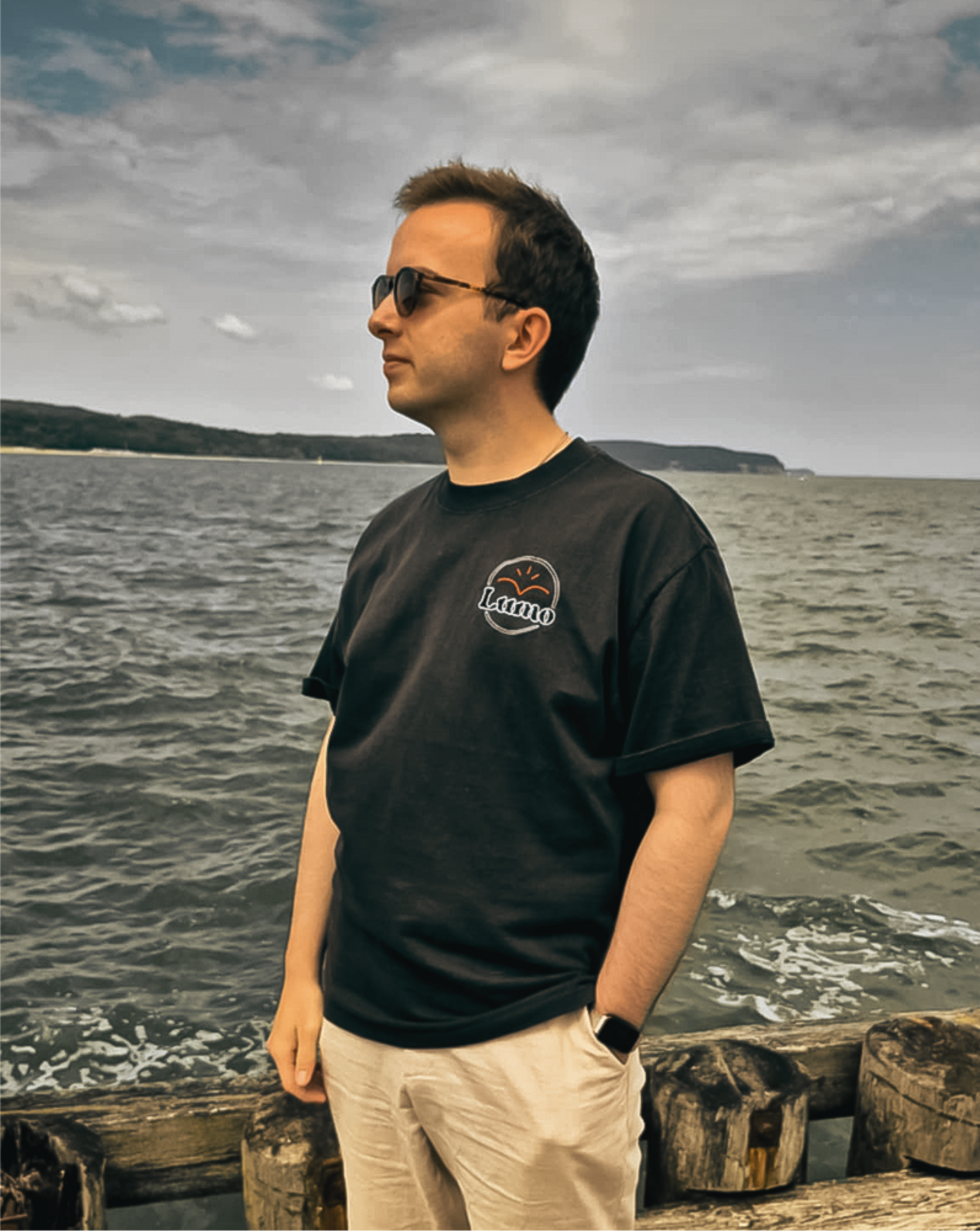 Man wearing a black t-shirt with a Lumo logo standing by a body of water.